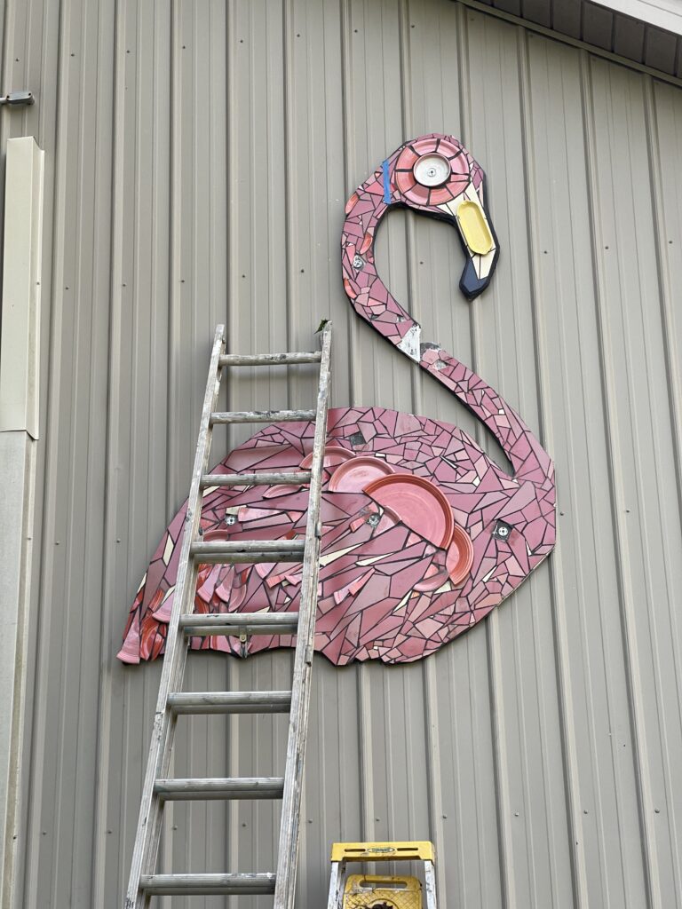 The image is a 6' moasic pink flamingo hanging on the side of the Bell Buckle Mosaic House.