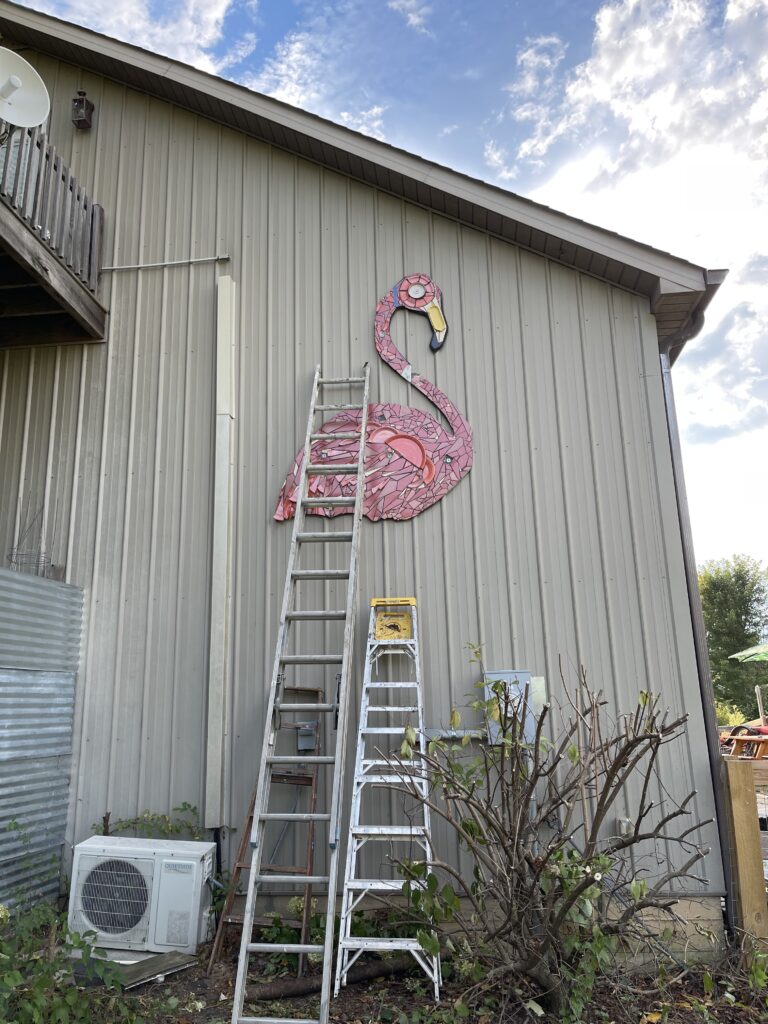 The image is a 6' moasic flamingo hanging on the side of the Bell Buckle Mosaic House.