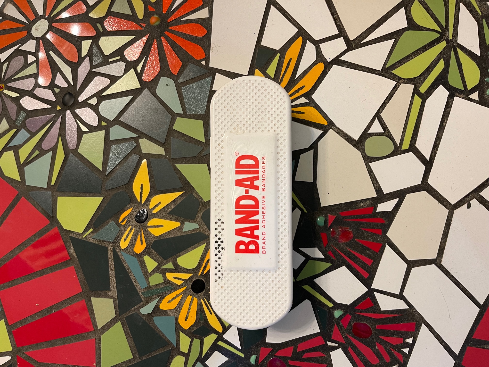 The image is a large white band-aid box on a mosaic floor.