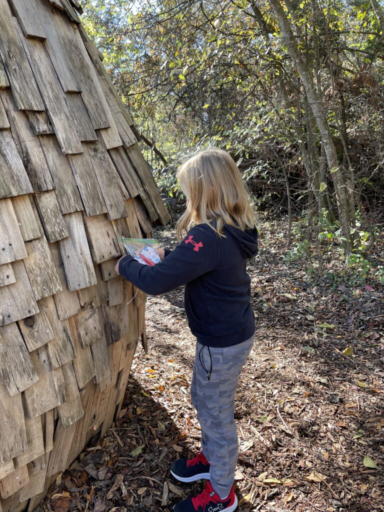 The image is of a young girl leaving a fabric heart with a message she and her sister had made with her grandmother to be found by someone else at the Giant Forest at Bernheim Arboretum and Research Forest.